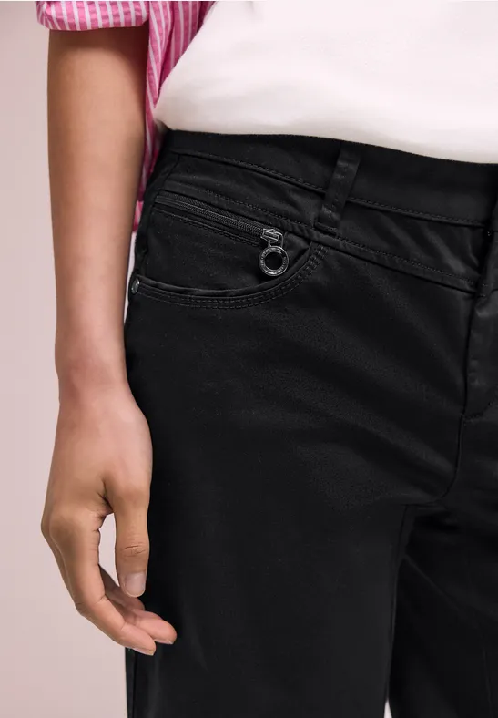 Close-up van persoon in zwarte jeans en roze-wit overhemd, hand ontspannen bij de heup.