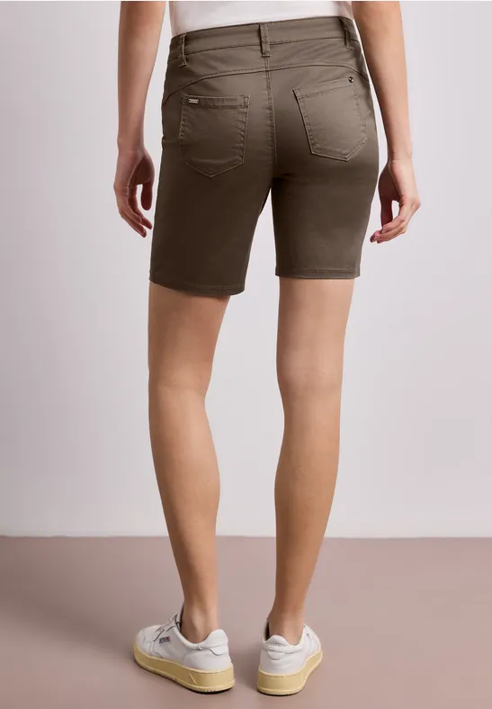 Achteraanzicht van een persoon in olijfgroene bermudashorts en witte sneakers tegen een neutrale achtergrond.