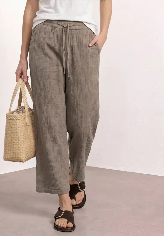 Losse kaki linnenbroek, wit topje, zwarte sandalen en een rieten tas.