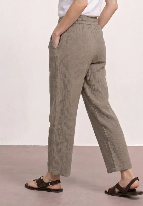 Zijaanzicht: losse, enkelhoge broek in licht olijfgroen met zijzakken en zwarte sandaaltjes.