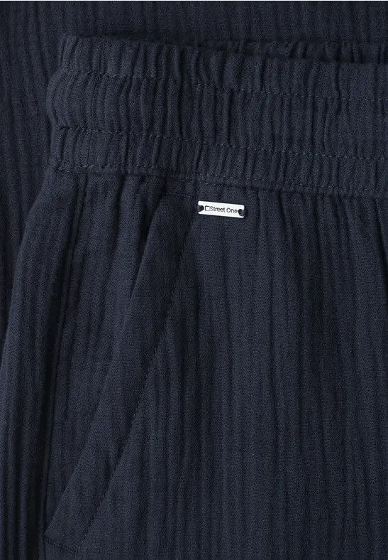 Dunkelblauer, leicht strukturierter Stoff mit elastischem Bund, seitlicher Tasche und kleiner Metallplakette