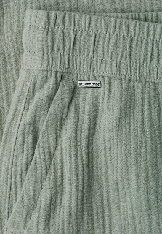 Close-up van een lichtgroene, gestructureerde broek met elastische taille, zijzak en klein merkembleem.