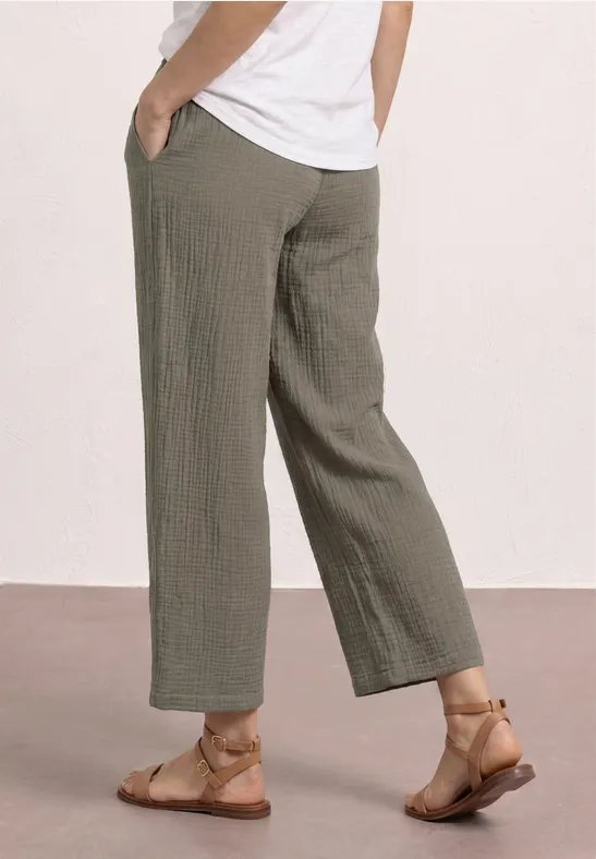 Eine Person trägt weite, knöchellange, olivgrüne Hosen und flache Sandalen.