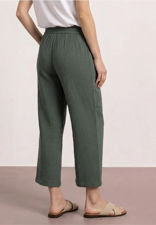 Vrouw van achteren in wijde, geribbelde olijfgroene broek net boven de enkel en sandalen.