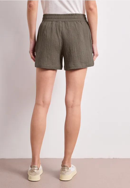 Femme de dos portant un short vert et des baskets blanches sur fond neutre