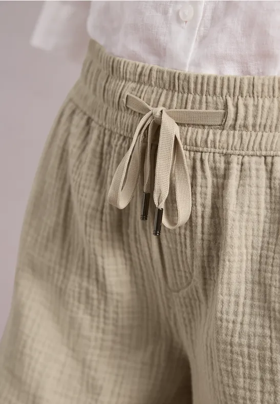 Beine im beigen, strukturierten Leinenhose mit Kordelzugbund und weißem Leinenhemd.