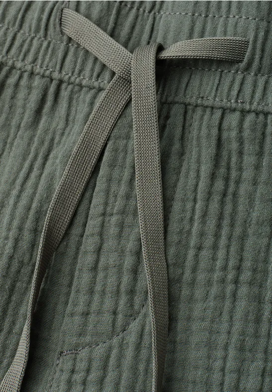 Nahaufnahme einer graugrünen, strukturierten Hose mit Kordelzug und seitlicher Tasche.