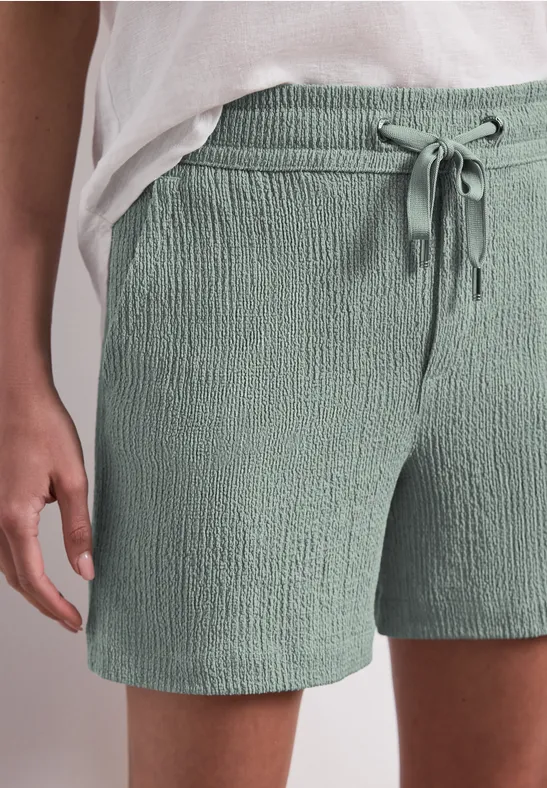 Person trägt mintgrüne, strukturierte Shorts mit Tunnelzug und weißem Oberteil.