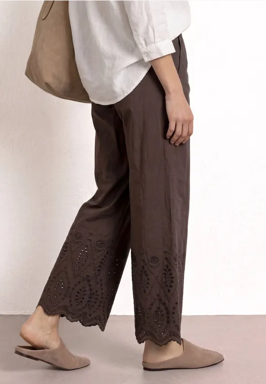 Vue latérale d'une personne portant un pantalon marron fluide à ourlet découpé, haut blanc, mocassins beige et sac.