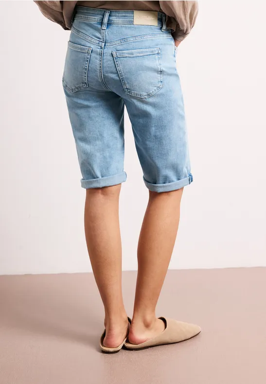 Achteraanzicht van een persoon in lichtblauwe, opgerolde jeansshort en beige pantoffels voor een neutrale achtergrond
