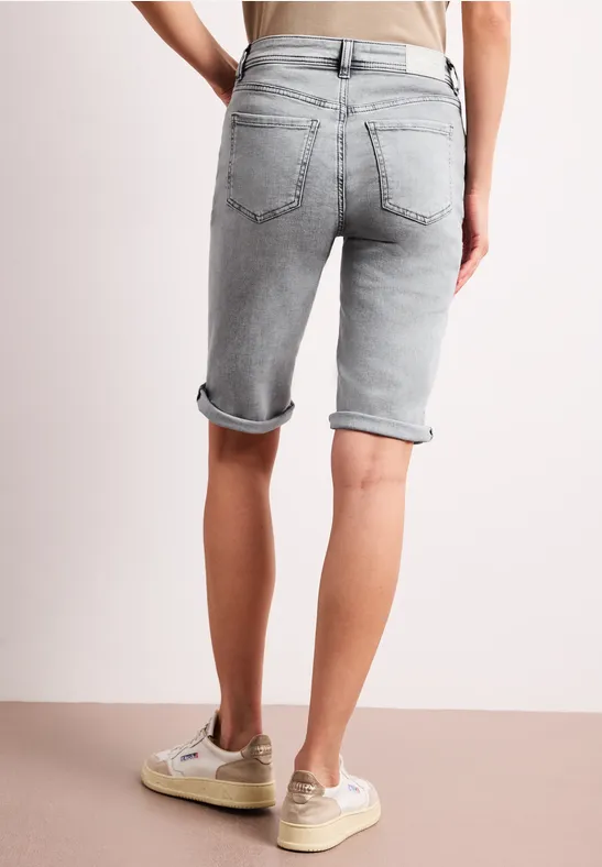 Rückansicht einer Person in grauen Jeans-Shorts mit umgeschlagenem Saum und beigen Sneakern.