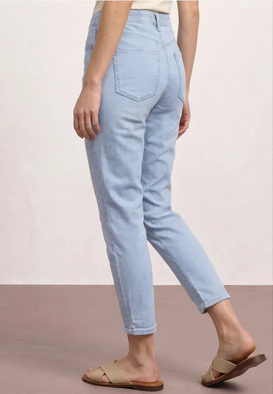 Vrouw van achteren in lichtblauwe spijkerbroek en beige sandalen.