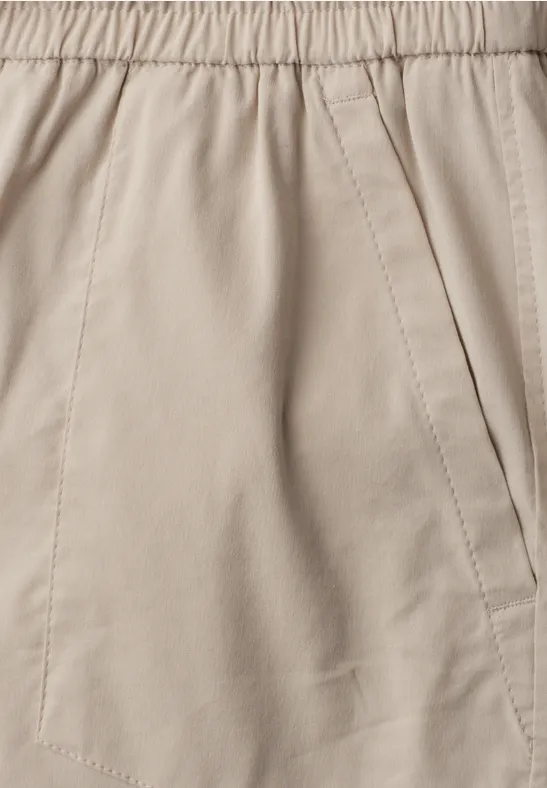 Detailansicht einer beigen Stoffhose mit elastischem Bund und seitlicher Eingrifftasche