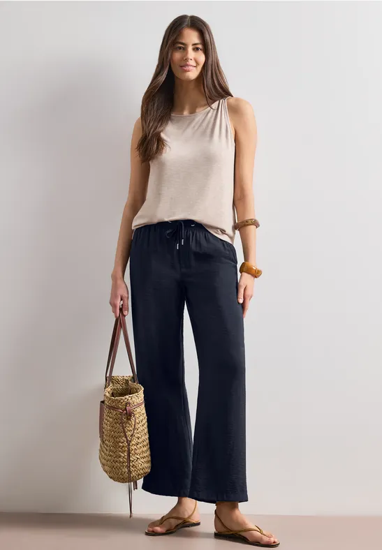 Frau in weitem Dunkelblau-Jeans, ärmellosem Top, Sandalen und Korbtasche.