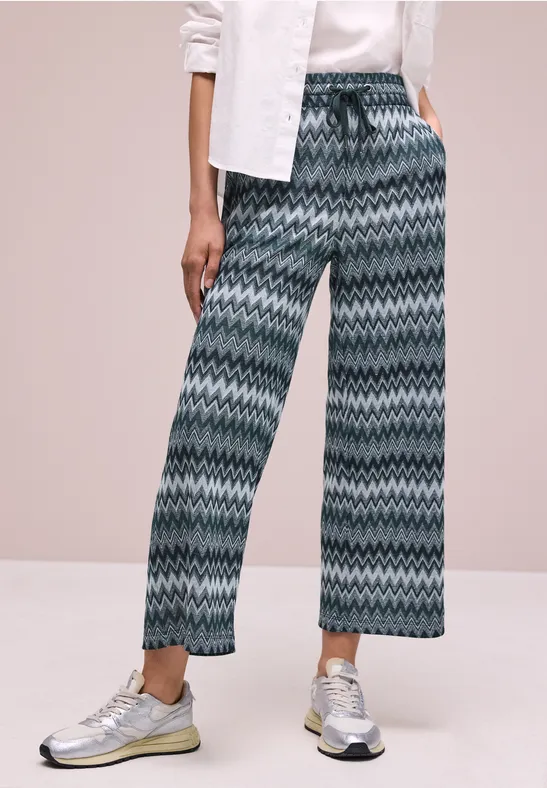 Wijde broek met groen-blauw zigzagpatroon, gecombineerd met witte sneakers.