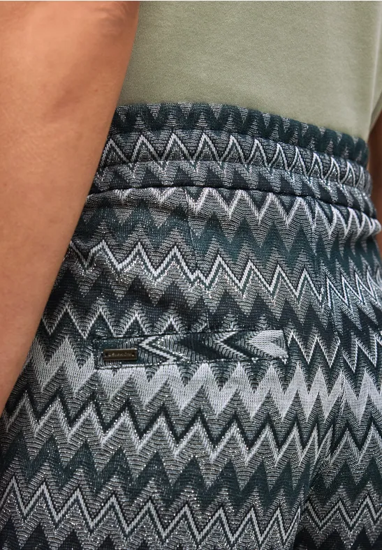 Nahaufnahme einer Rückansicht einer Person in blau-grauer, gezackter Hose mit Tasche und grünem Shirt.