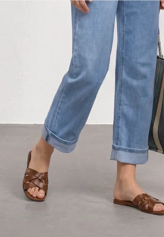 Füße in braunen, geflochtenen Ledersandalen und hochgekrempelten, hellblauen Jeans.