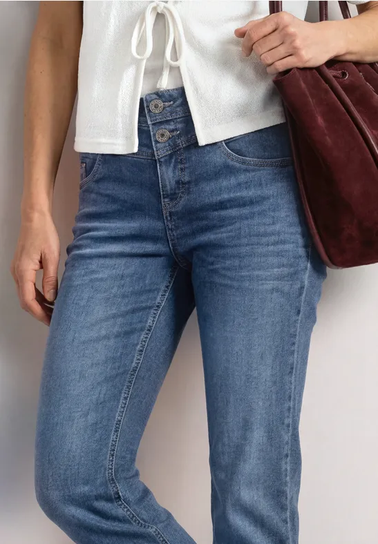Eine Person trägt blaue Jeans, ein weißes Oberteil und hält eine dunkelrote Tasche.