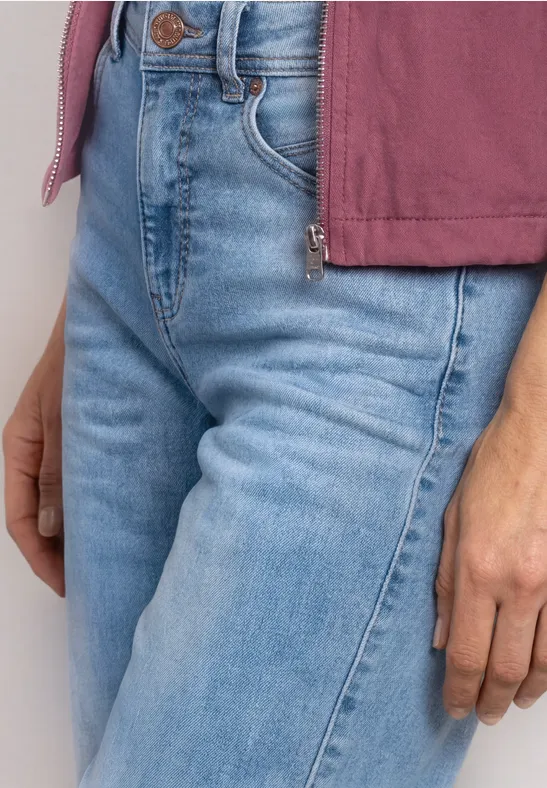 Eine Person trägt eine hellblaue Jeans und einen rosa Pullover, sichtbar sind Taille und Hand.