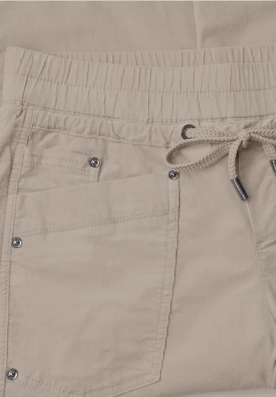 Beige Hose mit elastischem Bund, Kordelzug und aufgesetzter Tasche mit Metallnieten.