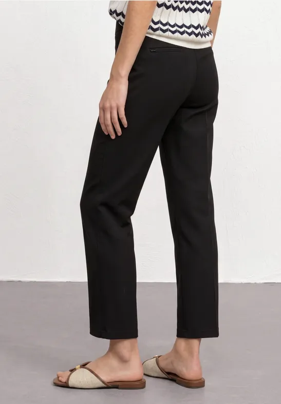 Schwarze, knöchellange Hose in geradem Schnitt, kombiniert mit beigen Pantoletten.