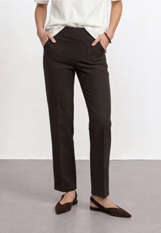 Schlanke schwarze Hose, weißes Oberteil, spitze Ballerinas, Hände in den Taschen.