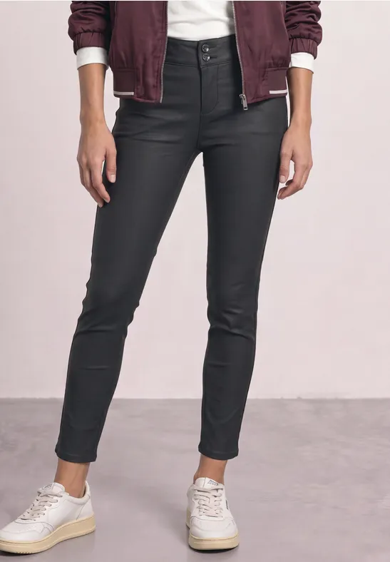 Jeans noires moulantes enduites, taille haute, ourlets aux chevilles et baskets blanches.