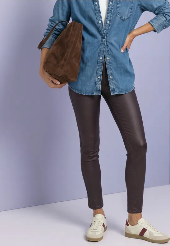 Eine Person mit Jeanshemd, schwarzen Lederleggings, weißen Sneakern und einer braunen Tasche.
