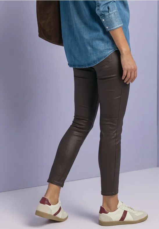 Frau trägt enge Lederhose, Jeanshemd, weiße Sneaker mit rotem Streifen und eine braune Tasche.