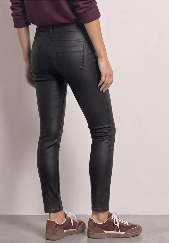 Eine Person steht von hinten, trägt enge schwarze Lederhose und weinrotes Oberteil.