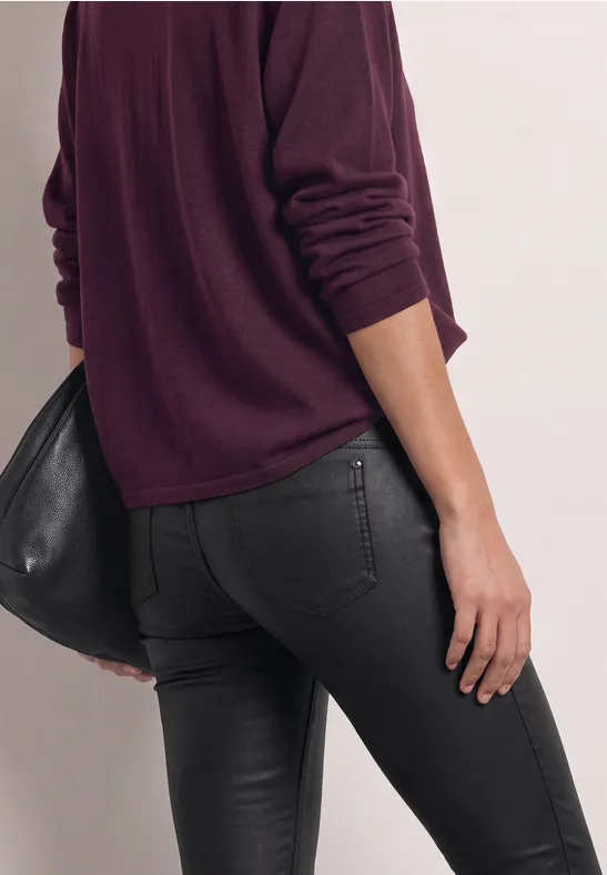 Von hinten sichtbare Person in lila Pullover und engen schwarzen Jeans, mit schwarzer Tasche.