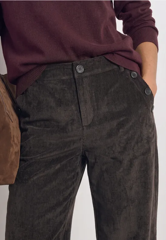 Dunkle Cordhose mit Knopfleiste, kombiniert mit einem kastanienbraunen Pullover.