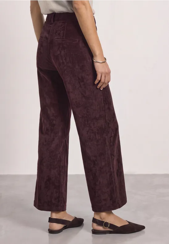 Rückansicht einer Frau in weinroter Cordhose mit weitem Bein und schwarzen Ballerinas.