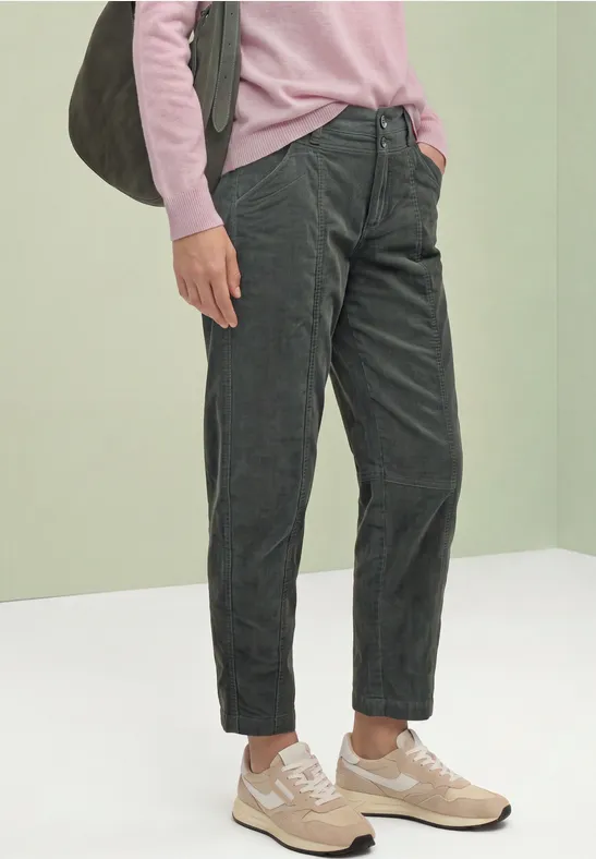 Person trägt pinken Pullover, dunkelgraue Cordhose, beige Sneaker und graue Schultertasche.
