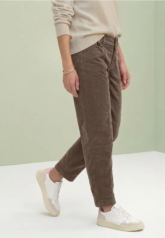 Persoon met beige trui, bruine corduroy broek en witte sneakers voor lichte achtergrond.