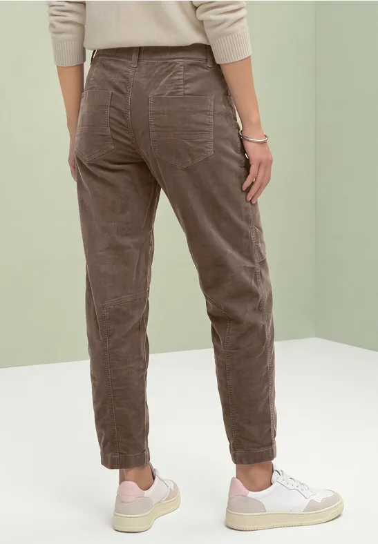 Persoon van achteren in bruine corduroy broek en witte sneakers voor een lichte achtergrond.