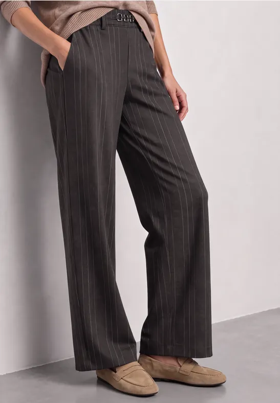 Frau trägt dunkelgraue Nadelstreifen-Hose mit weitem Bein und hellbeigen Loafers.