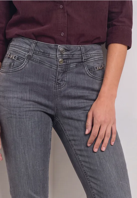 Eine Frau trägt graue Jeans und ein dunkelrotes Oberteil, nur Rumpf und Hand sind zu sehen.