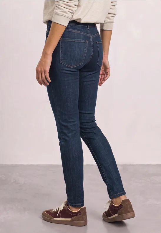 Person trägt dunkle Skinny-Jeans und braune Schuhe, steht seitlich vor heller Wand.