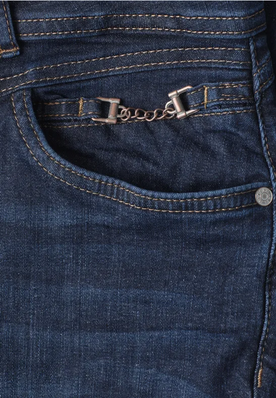 Nahaufnahme einer blauen Jeans mit dekorativer silberner Kette am vorderen Hosentaschensaum.