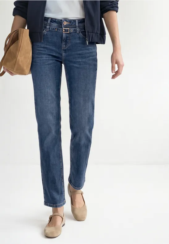 Frau in blauen Jeans, weißem Shirt, navyblauer Jacke und beigen Schuhen mit Tasche.