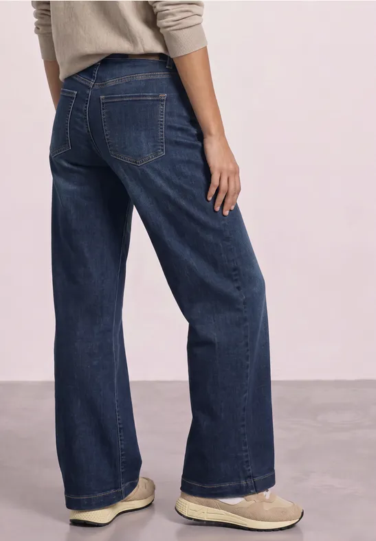 Rückansicht einer Person mit weitem, dunkelblauen Jeanshose und hellen Schuhen.