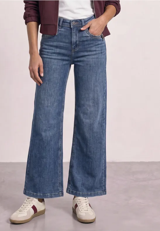 Frau trägt hoch taillierte, weit geschnittene Jeans, weiße Sneaker und eine burgunderrote Jacke.