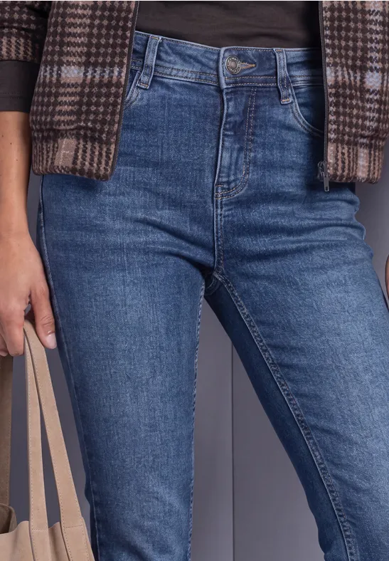 Person in blauen High-Waist-Jeans, Karomuster-Cardigan, schwarzem Shirt und beiger Tasche.