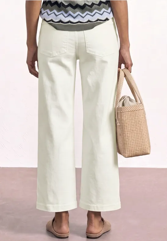 Frau von hinten in weißen Schlaghosen, gemusterter Bluse, Sandalen und Strohtasche