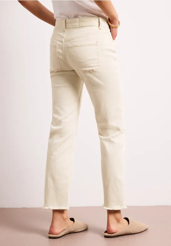Persoon draagt crème kleurige high-waist jeans met rechte pijpen en beige slippers.