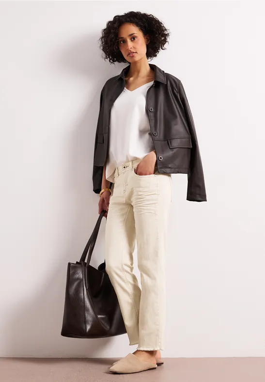 Persoon met zwarte leren jas, wit topje, beige broek en grote zwarte tas.