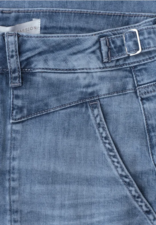 Blauer Jeansstoff mit Tasche, Bund und seitlicher Schnalle in Nahaufnahme.