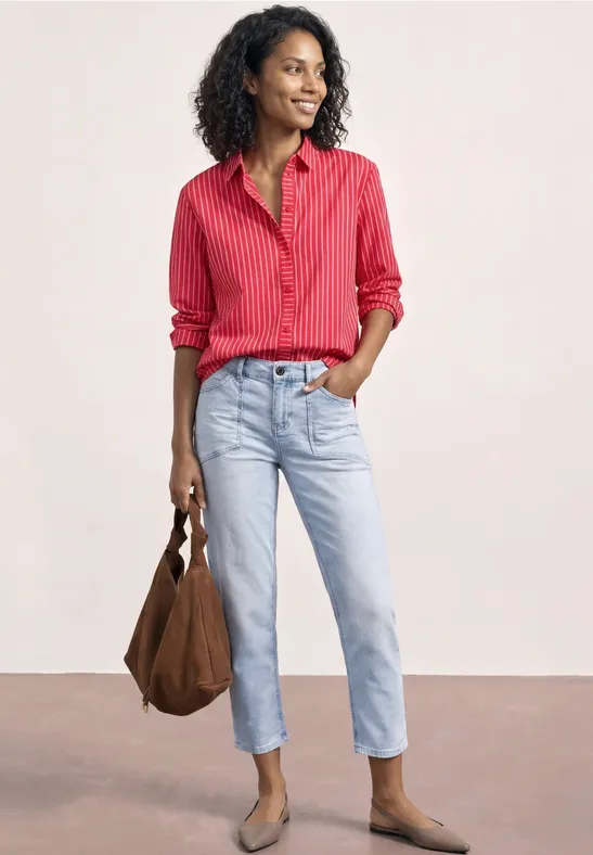 Frau in roter gestreifter Bluse und hellblauen Jeans mit brauner Tasche und beigen Schuhen.