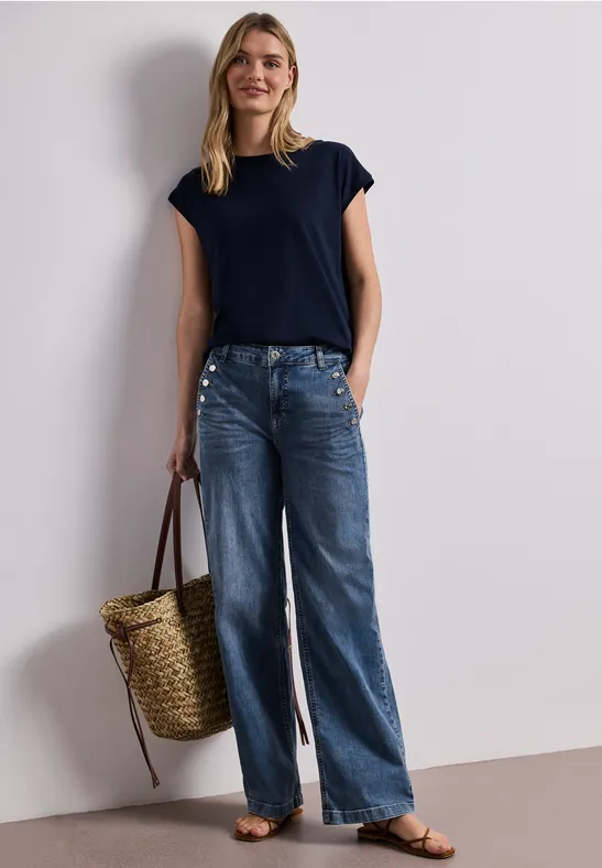 Femme en t-shirt bleu marine, jean ample, sandales plates, tenant un panier en osier.